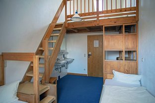 Blick in einen Übernachtungsraum mit Betten, Waschbecken und Treppe